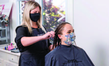 Hair stylist cutting a woman's hair while wearing a mask
