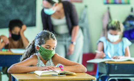 Young girl wearing mask sitting at school desk in a classroom