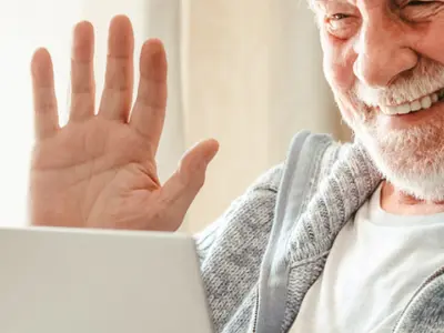 Picture of a man in his 70s, waving to someone on the screen. 