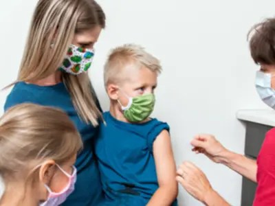 Child getting vaccinated by nurse with mom and sibling there too