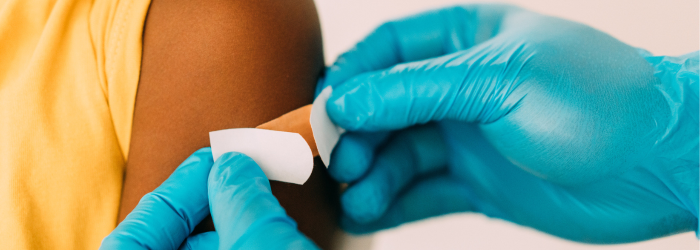 Health care provider putting bandaid on arm of child after immunization. 