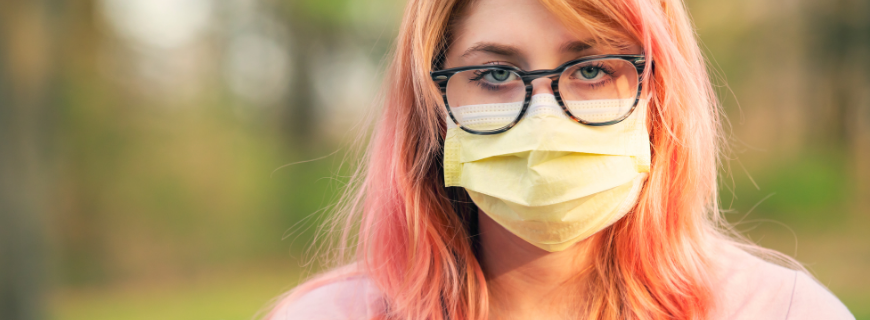 Teenager with pink hair wearing a face covering.