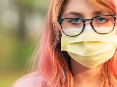 Teenager with pink hair wearing a face covering.